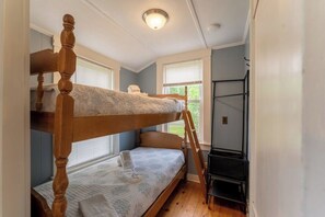 A bunk bed with a ladder, a desk, and a window with blinds.