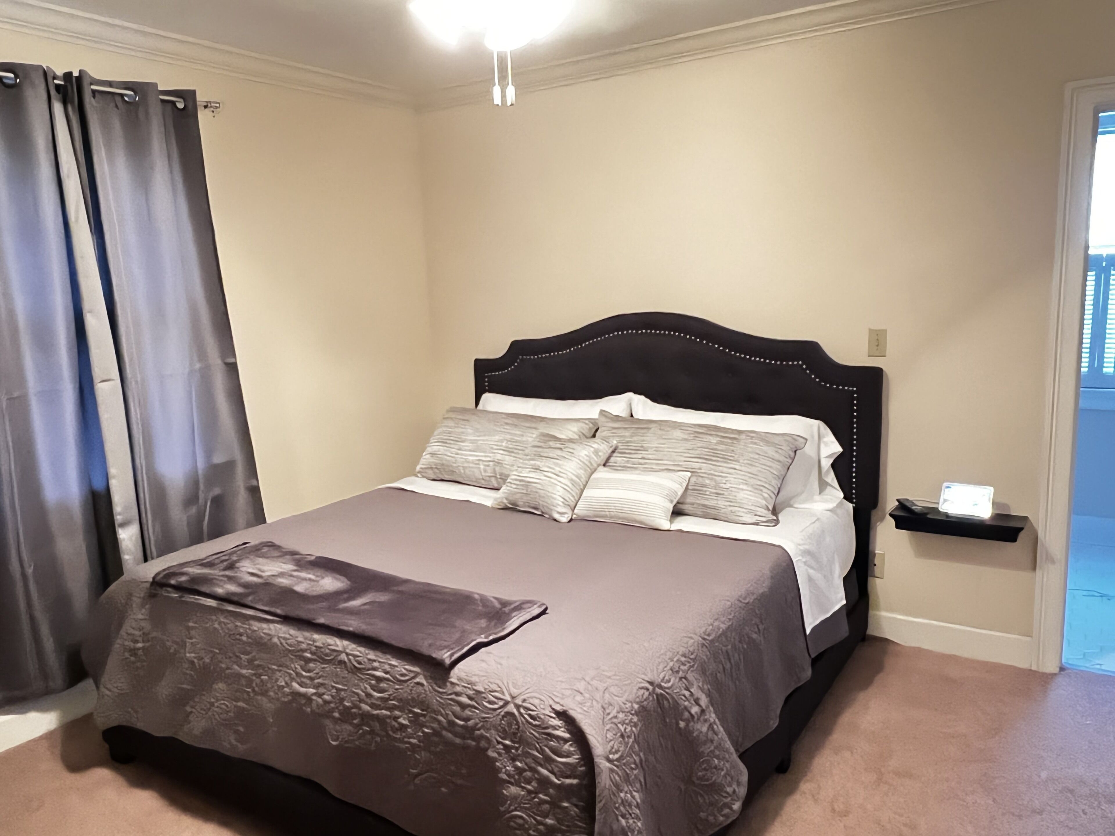 Un dormitorio con cama, cortinas, una mesita de noche y un velador.