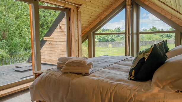 Een slaapkamer met een houten plafond, grote ramen en een bed met kussens.