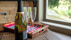 Een fles champagne, twee glazen en een kleurrijk dienblad op een houten tafel bij een raam.