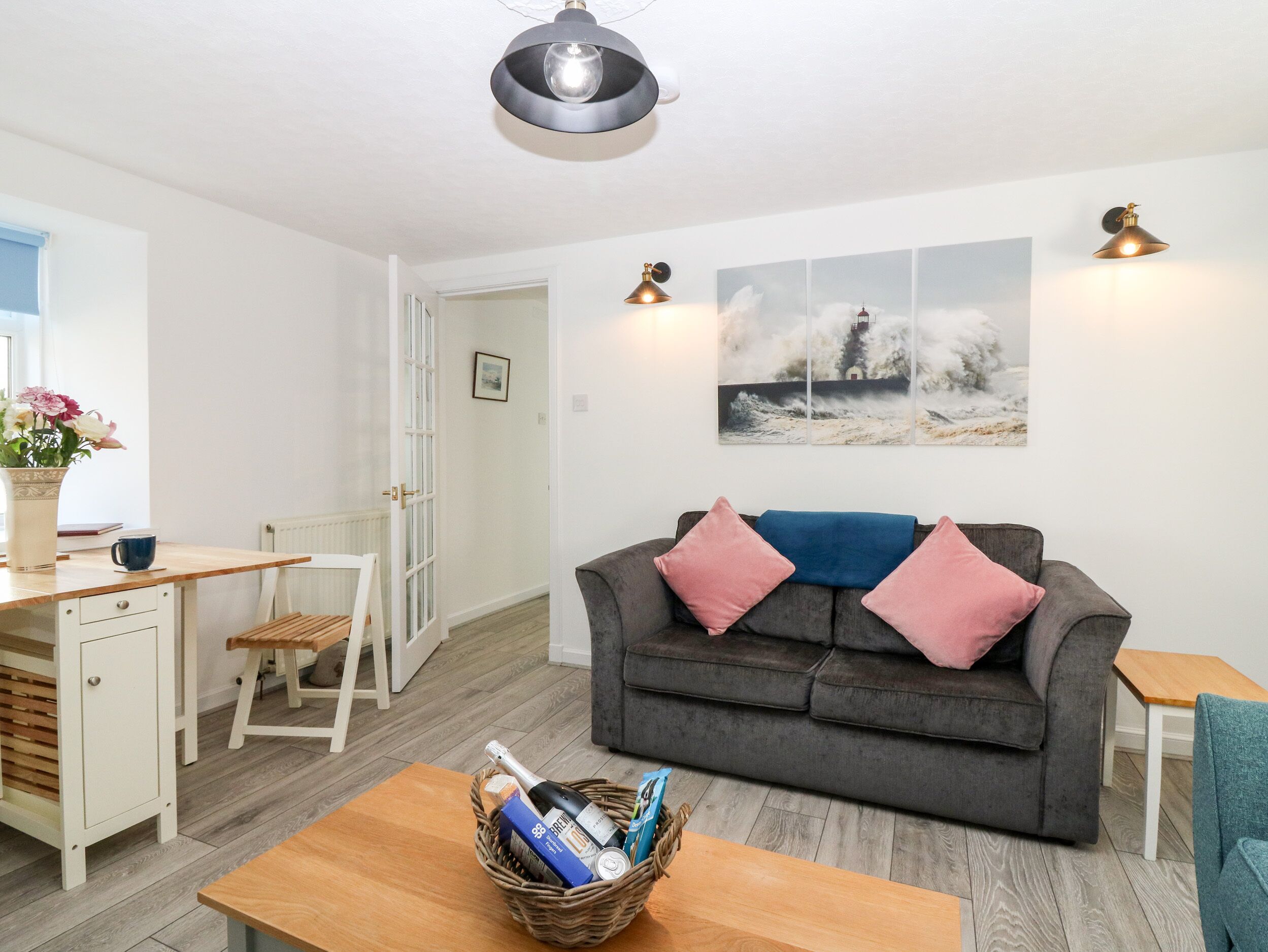 Ein modernes Wohnzimmer mit einem grauen Sofa, einem Holztisch und einem Korbkorb mit Flaschen.