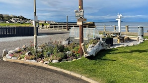 Une promenade en bord de mer, agrémentée d’un panneau indicateur, d’un espace de repos abrité et offrant une vue sur la mer.