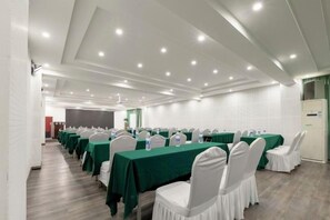 Un salón de conferencias con filas de mesas, sillas y una pared de ladrillo blanco.