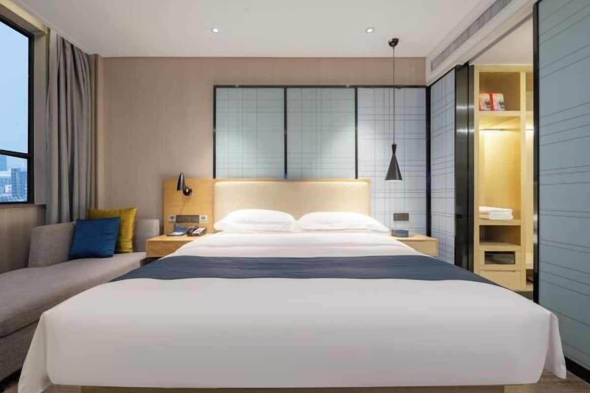 Une chambre d’hôtel moderne avec un grand lit, des tables de chevet, un canapé et une vue sur la ville.