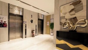 Eine moderne Lobby mit Marmorboden, Aufzügen, einer Rezeption und einem großen abstrakten Kunstwerk.