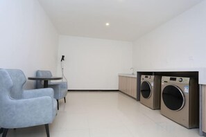 A laundry room with two washing machines, a small table, and two chairs. - Jinhua Tian Hotel (Hanchuan)