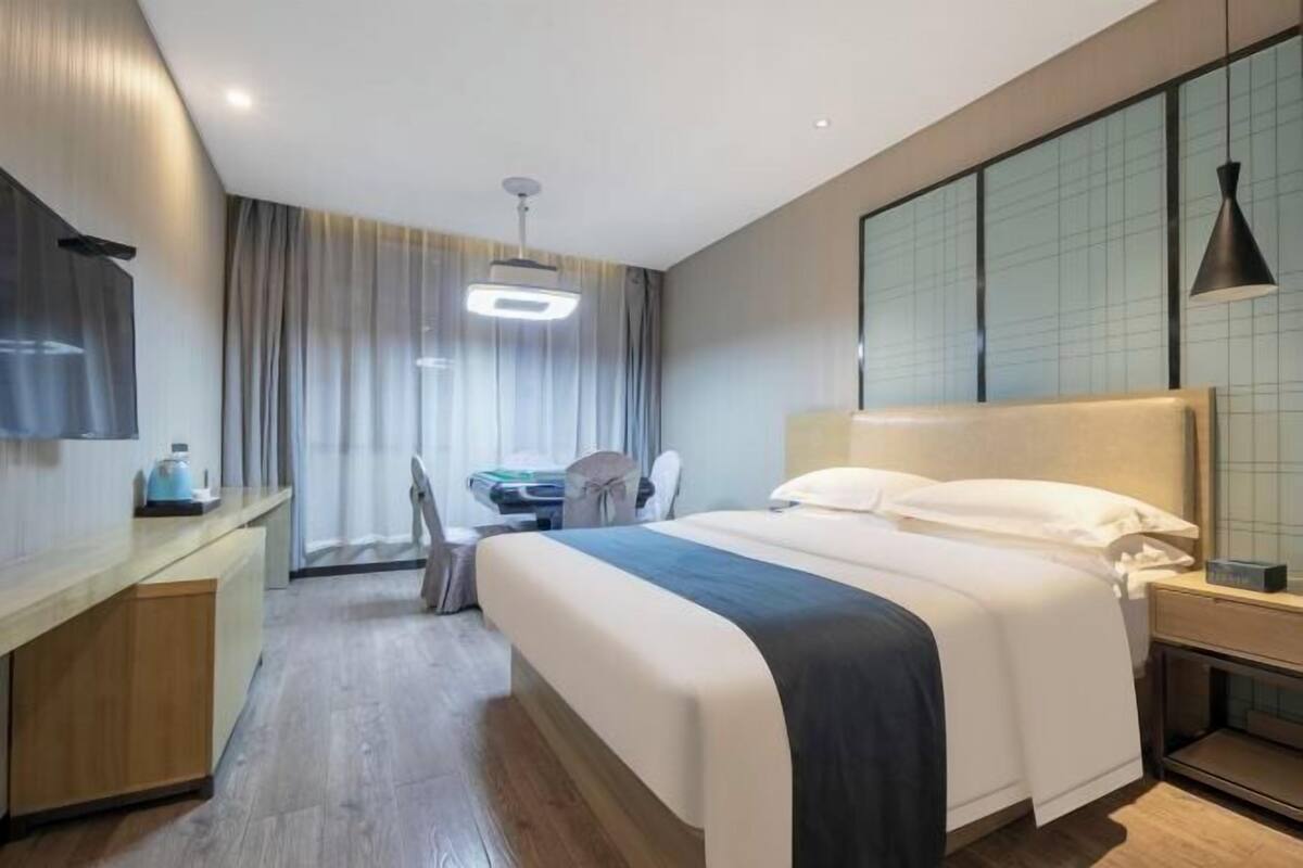 Une chambre d’hôtel comprenant un lit, une table de chevet, un bureau, une chaise et une grande fenêtre avec des rideaux.
