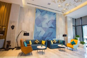 En moderne hotellobby med en hjørnesofa, to lænestole, et sofabord og et stort abstrakt vægmaleri.