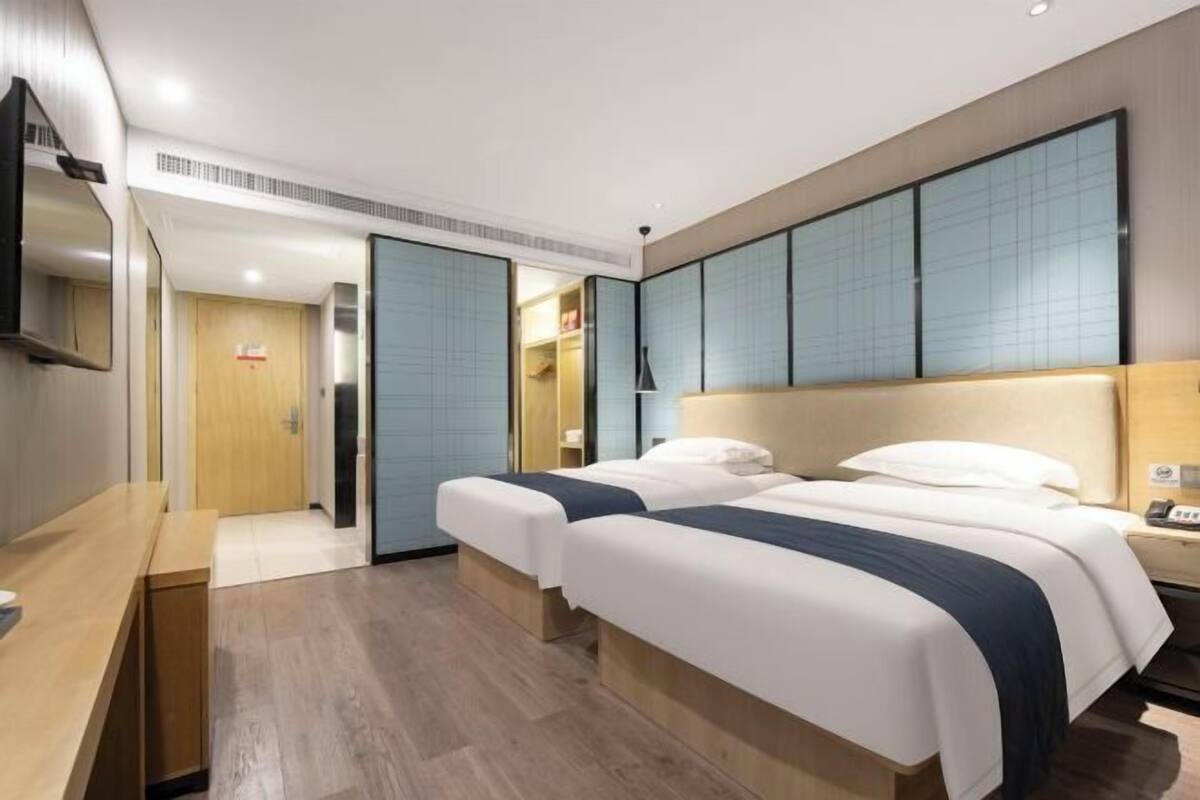 Une chambre d’hôtel avec deux lits, un bureau en bois, une télévision et une grande fenêtre.