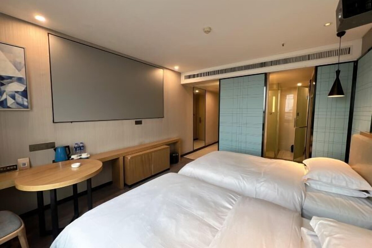 A modern hotel room with a large bed, a small desk, and a mirror.