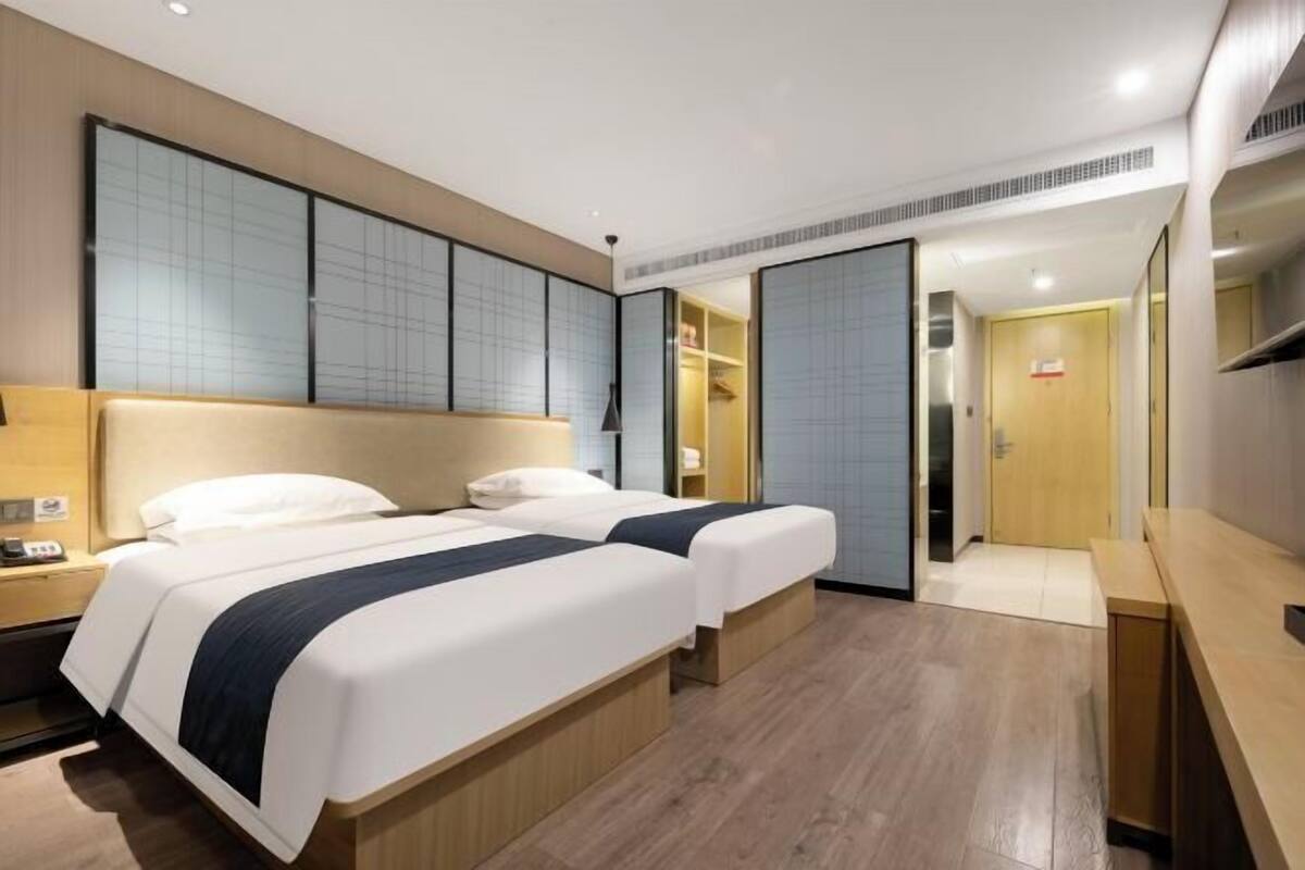 Une chambre d’hôtel avec deux lits, un bureau, une armoire et une porte coulissante donnant accès à la salle de bain.