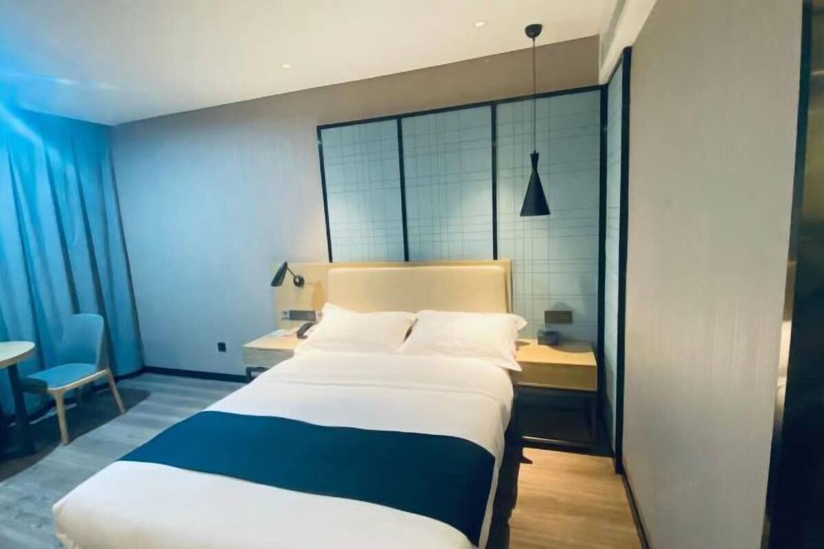 Une chambre d’hôtel moderne, équipée d’un lit, de tables de chevet, d’un bureau, d’une chaise et d’une grande fenêtre avec des stores.