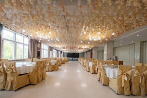 Une salle de banquet avec des tables dressées pour des événements, de grandes fenêtres et un plafond décoré de motifs floraux.