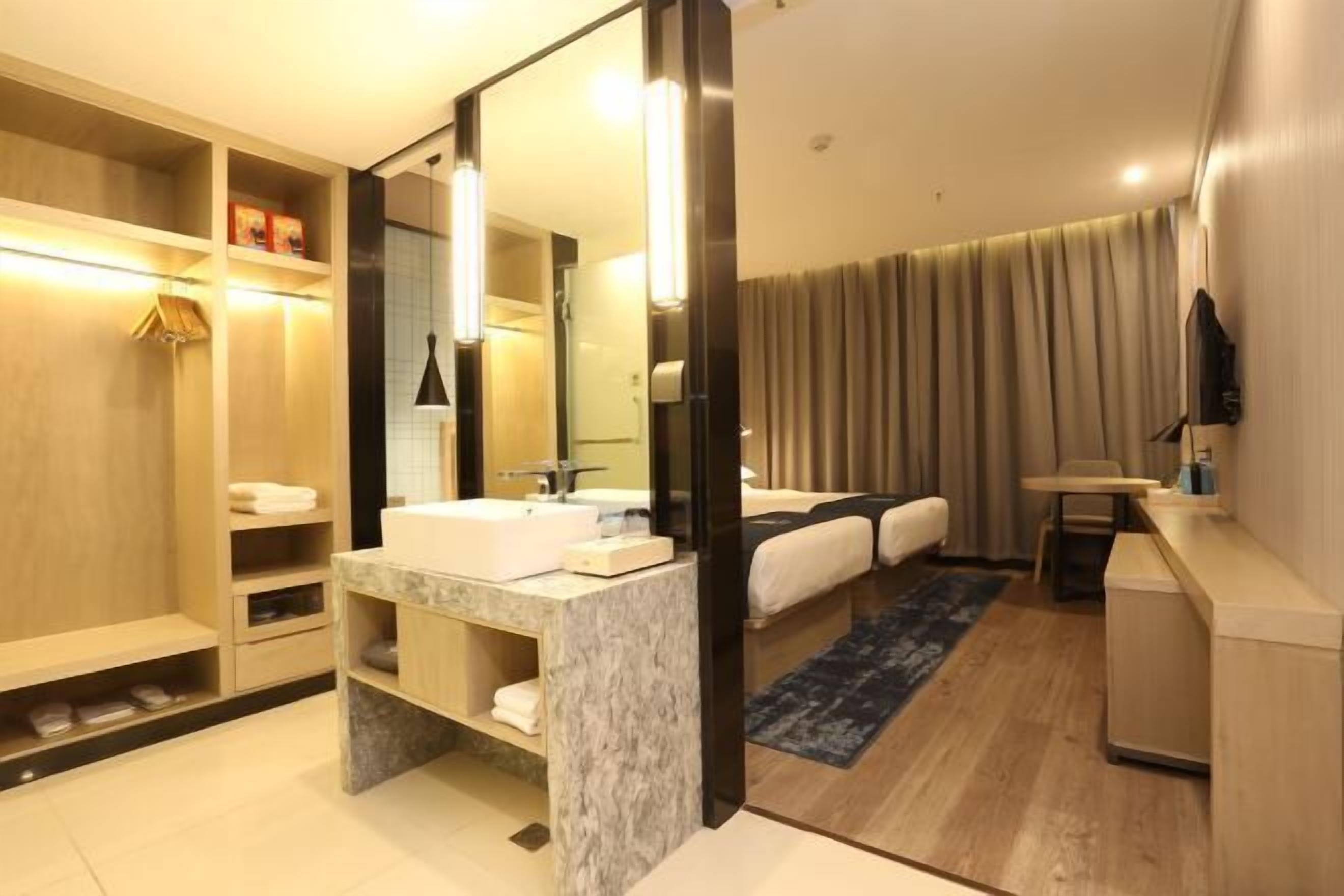 A modern hotel bathroom with a marble sink, a large mirror, a shower area, and a seating area with a blue rug.