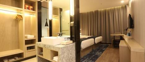 A modern hotel bathroom with a marble sink, a large mirror, a shower area, and a seating area with a blue rug.