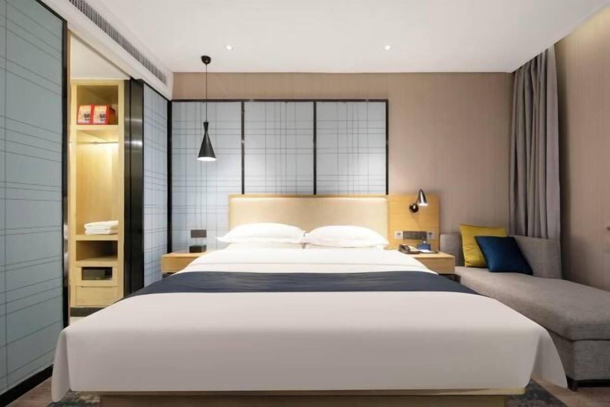 Une chambre d’hôtel moderne avec un grand lit, des tables de chevet, une armoire et une vue sur la ville.