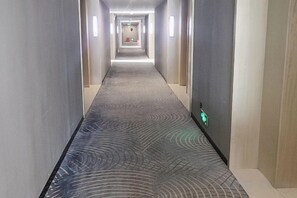 Un long couloir étroit, typique des hôtels, avec un tapis à motifs et des murs de couleur claire.