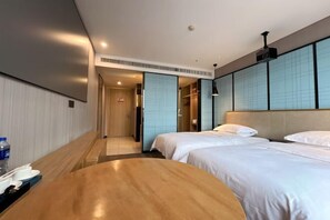 Ein Hotelzimmer mit zwei Betten, einem Holztisch, einer Minibar und einem Badezimmer mit Schiebetür.
