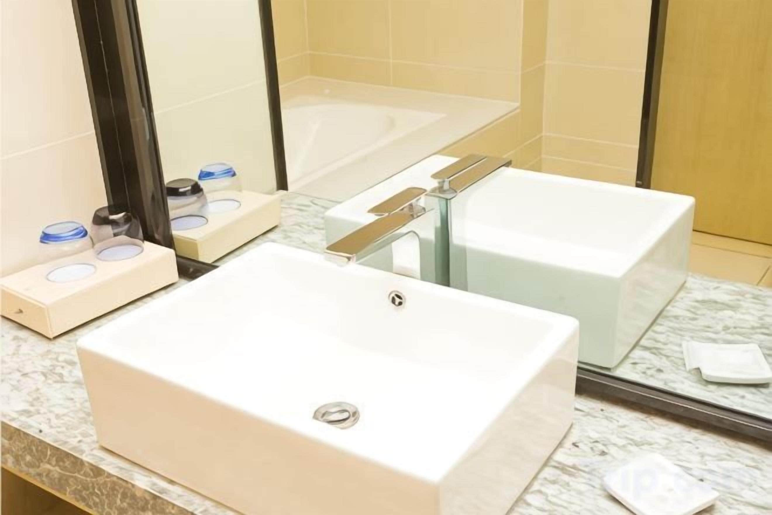 Un baño con lavamanos blanco, espejo, bañera y encimera de mármol.