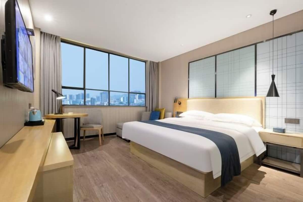 Une chambre d’hôtel avec un grand lit, un bureau, une chaise, une télévision et une vue sur la ville.