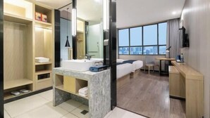 Ein modernes Hotelzimmer mit einem großen Bett, einem Schreibtisch, einem Badezimmer mit Waschtisch und Blick auf die Stadt.