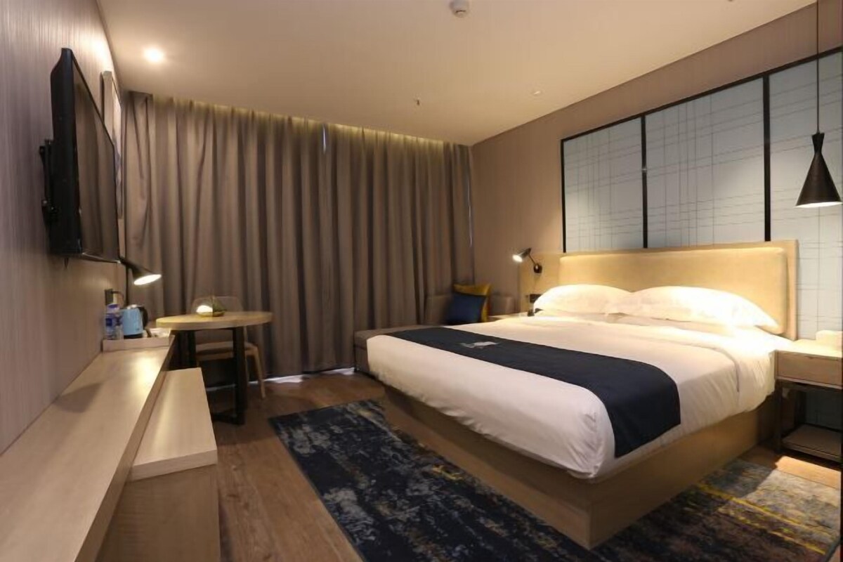 A modern hotel room with a large bed, bedside tables, a desk, and a flat-screen TV mounted on the wall.