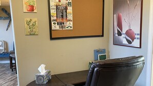 Una sala de conferències amb una taula de fusta, una cadira de cuir negre, un tabló d'anuncis amb diversos avisos i un quadre abstracte amb marc.