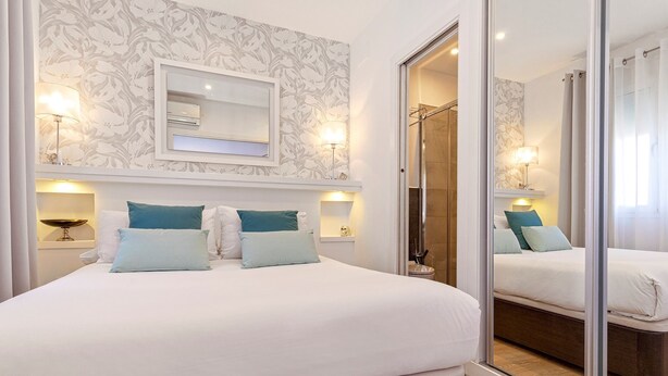 Un dormitorio con una cama grande, dos mesitas de noche con lámparas, un espejo sobre la cama y un ventanal corredero que da a un baño.