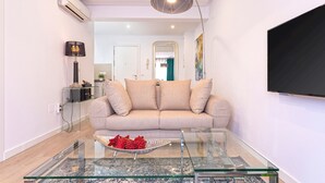 Una sala de estar moderna con una mesa de centro de vidrio, un sofá color beige y un televisor de pantalla plana montado en la pared.