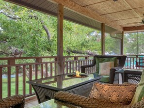 Un patio exterior con mobiliario de mimbre, una mesa de vidrio y una chimenea.