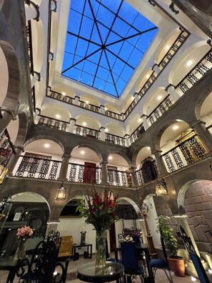 Interior de hotel con un atrio central, varios balcones con barandas de hierro forjado y un tragaluz.