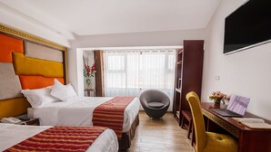 Ein Hotelzimmer mit zwei Betten, einem Schreibtisch mit einem Laptop, einem Stuhl und einem an der Wand befestigten Fernseher.
