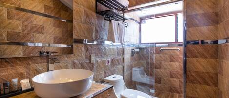 A modern bathroom with a large vessel sink, a toilet, and a glass shower enclosure.