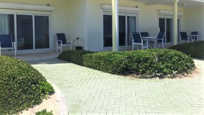 Un hotel con un patio empedrado, mobiliario exterior con sillas y mesas, y un balcón con barandillas blancas.