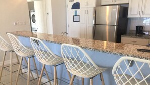 Una cocina con encimera de granito, electrodomésticos de acero inoxidable y taburetes de bar blancos.