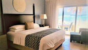 Habitación de hotel con una cama grande, una mesita de noche, una lámpara y vistas al océano a través de la ventana.