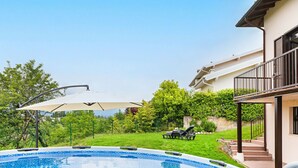 A swimming pool with a tiled edge, surrounded by a grassy area and trees. There is a covered seating area with a table and chairs. - Fantastic Villa in Soiano del Lago  for 6 people with pool  (Soiano del Lago)