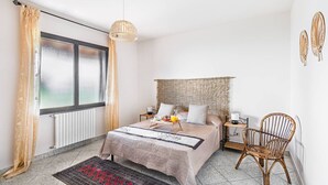 A bedroom with a bed, bedside tables, a chair, a window with curtains, a hanging light fixture, and a radiator. - Fantastic Villa in Soiano del Lago  for 6 people with pool  (Soiano del Lago)