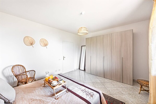 A bedroom with a bed, a wicker chair, a bedside table with breakfast items, and a wardrobe. - Fantastic Villa in Soiano del Lago for 6 people with pool (Soiano del Lago)