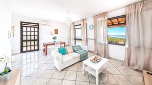 A spacious living room with a white sofa, a dining table, and a view of the sea. - Fantastic Villa in Soiano del Lago  for 6 people with pool  (Soiano del Lago)