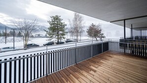 Eine Holzterrasse mit Metallgeländer, mit Blick auf eine verschneite Straße mit parkenden Autos und Bäumen.
