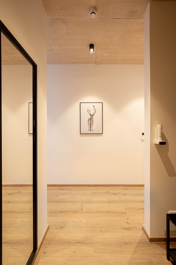 Un couloir avec un plancher en bois, une œuvre d’art encadrée au mur et une machine à café sur la droite.