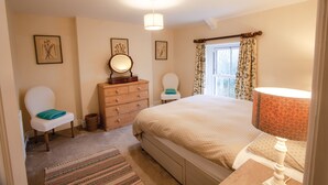 A bedroom with a large bed, a dresser, a chair, a mirror, and a window with curtains.