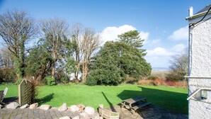 A patio area with a stone table, a bench, and a picnic table. There are rocks and a small garden area with a lawn.