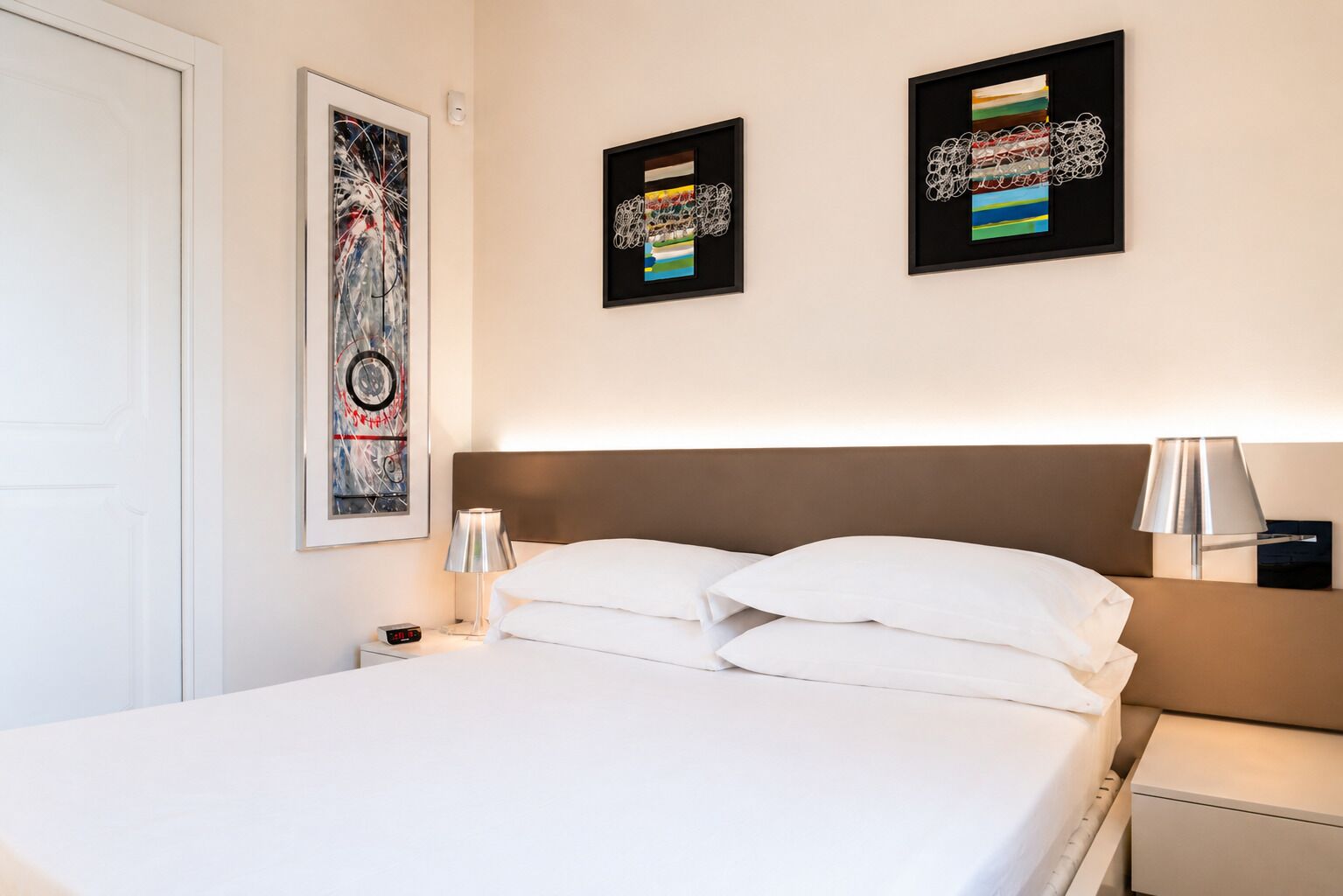 Une chambre d’hôtel avec un lit, une table de chevet, une lampe et deux œuvres d’art encadrées accrochées au mur.