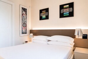 A hotel room with a bed, a nightstand, a lamp, and two framed artworks on the wall.