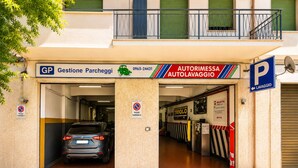 Un'auto parcheggiata all'ingresso di un edificio con un cartello che indica 'Gestione Parcheggi' e 'Autorimessa Autolavaggio'.