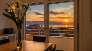Una stanza con un tavolo da pranzo, un vaso con fiori e vista sul tramonto su un corpo d'acqua con edifici sullo sfondo.