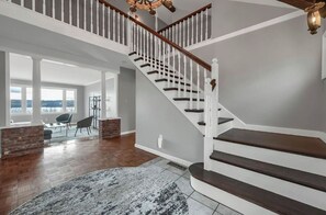 Stunning interior with a grand staircase, high ceiling, and large windows offering views of the outdoors.