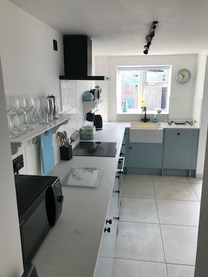 A modern kitchen with white cabinets, a black range hood, a window with a view, and a clock on the wall.